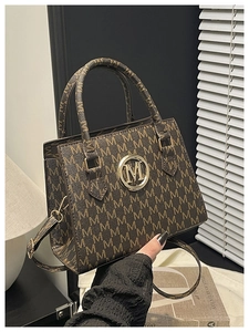 Dettaglio di una borsa a tracolla marrone con stampa a lettere M e logo metallico dorato