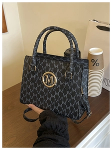 Detailed macro view of black crossbody bag featuring repeat M letter patterns and gold hardware
