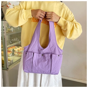Detail of purple pleated tote bag with three front pockets and metal snaps in a street setting