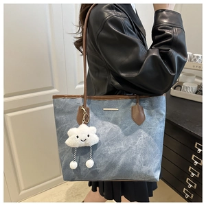 Blue denim tote bag with brown leather straps and plush cloud pendant worn by a model