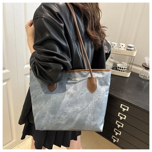 Detail of blue denim tote bag featuring brown leather trim and golden metal buckle
