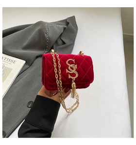 Détail d'un sac matelassé en velours rouge avec logo S doré et pendentif à franges
