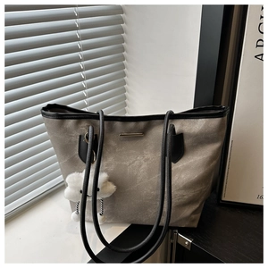 Detail of grey tote bag featuring slim shoulder straps and a white plush cloud charm accessory