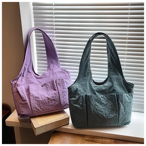 Detail view of nylon tote bag showing triple front pockets and metallic buckles