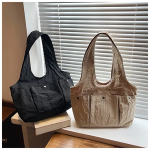 Detail view of khaki and black pleated nylon tote bags with three front pockets and metal snaps