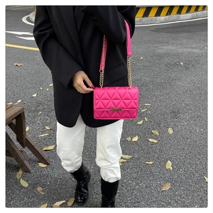 Outdoor shot of bright pink quilted crossbody bag with gold chain strap and metal trim