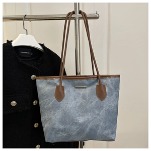 Close-up of denim tote bag featuring brown leather trim and gold metal hardware detail