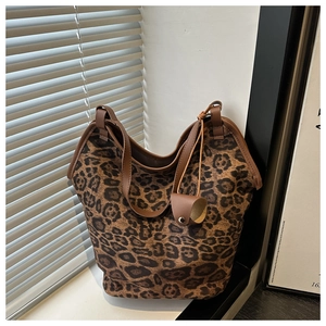 Detail of leopard print tote bag with brown leather handle and cylindrical charm hanging