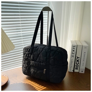 Detail of black quilted shoulder bag featuring embroidered heart patterns and front zipper