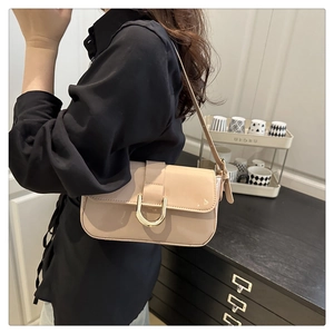 Beige patent leather underarm bag with gold horseshoe buckle worn by a model in a room