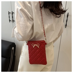 Detail of red quilted phone bag with gold bow clasp and elegant chain strap on a white outfit