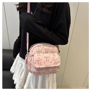 Détail du sac bandoulière en velours côtelé rose avec nœuds rouges et sangle réglable