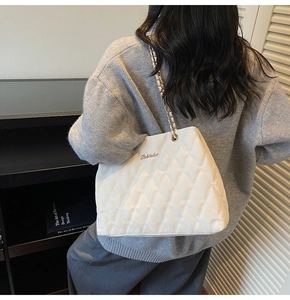 Details einer weißen Stepptasche mit goldener Kette und metallischem Markenlogo