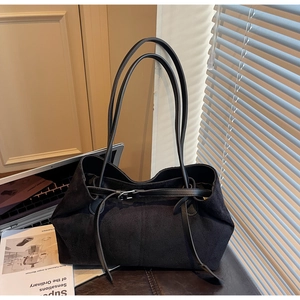 Detail shot of black suede tote bag with slim shoulder straps and metal buckle on leather mat