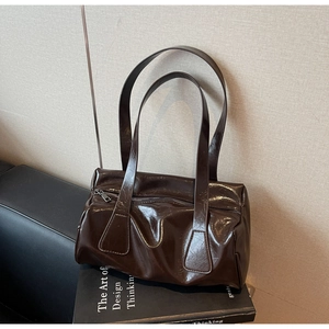 Detailed view of dark brown gloss leather baguette bag placed on an art book