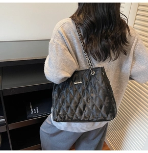 Detail of black quilted shoulder bag featuring silver chain strap and metal logo accent