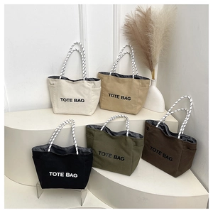 Collection of canvas tote bags in five colors with rope handles on white display stand