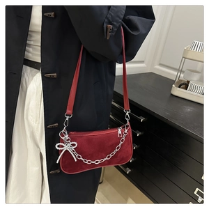 Detail of red suede baguette bag with silver chain strap and beaded butterfly charm