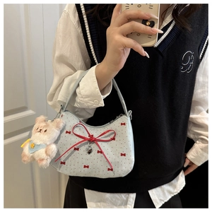 Gros plan d'un sac à main bleu clair avec des nœuds rouges, pendentif cœur et ours en peluche