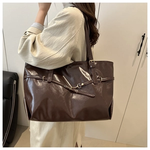 Detail of dark brown tote bag featuring glossy leather and gold buckle strap decoration