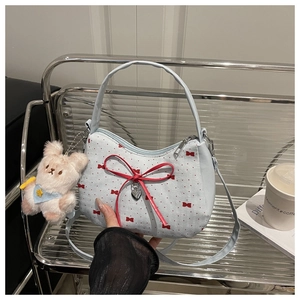 Détail du sac à main bleu clair avec nœuds rouges, breloque cœur et lapin en peluche