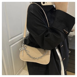 Detail view of beige crescent bag with silver chain and bow charm on a model shoulder