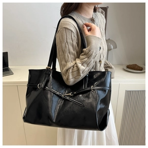Detail of glossy black leather tote bag with gold buckle and smooth texture finish