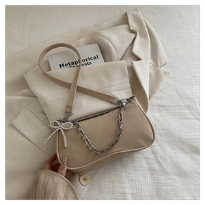 Vue détaillée du sac baguette en cuir beige avec chaîne argentée et nœud perlé