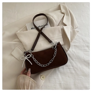 Détail du sac bandoulière en daim marron avec chaîne argentée et pendentif perle