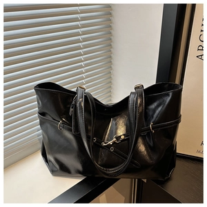 Close-up of black oily leather tote bag with glossy finish and gold metal eyelet details
