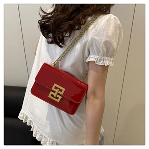 Detail of red glossy crossbody bag with gold chain strap and geometric lock worn by model