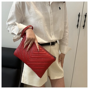 Detail of red quilted clutch with metallic studs and leather wristlet on white shirt
