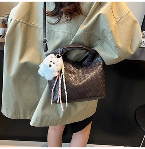 Detail of dark brown woven leather tote with white puppy charm and braided strap