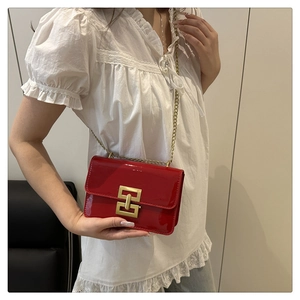 Detail view of red patent leather crossbody bag with golden chain and H-shaped buckle