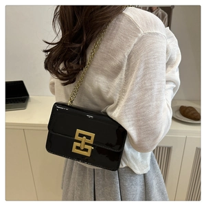 Detail of a black patent leather crossbody bag with a gold geometric lock and chain strap