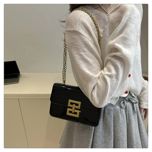 Detail of a chic black patent leather bag featuring a gold chain strap and geometric lock