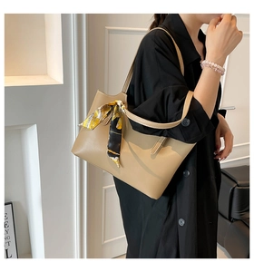 Detail of a beige tote bag with a silk scarf tied to the handle worn by a model