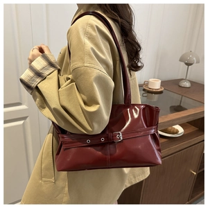 Detail view of burgundy glossy leather tote bag featuring silver buckle strap decorations