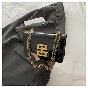 Detail of glossy black patent leather shoulder bag with gold chain and square buckle