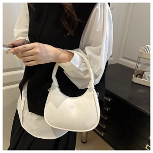 Detailed close-up of white crescent shoulder bag featuring stamped gold-tone fashion lettering