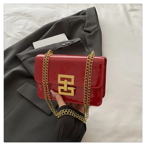 Detailed view of red patent leather texture and interlocking gold buckle on a crossbody bag