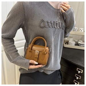 Detail of a brown mini messenger bag with silver pin buckle and delicate chain strap