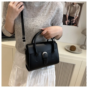 Model wearing a black leather handbag with silver buckle and adjustable shoulder strap