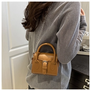 Detailed view of brown leather crossbody bag with silver buckle and chain strap on model