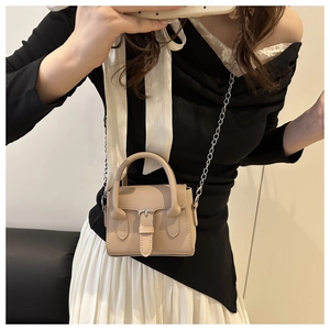 Detail of beige mini crossbody bag featuring a metal chain strap and buckle design