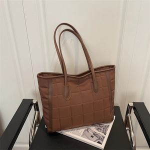 Quilted dark brown tote bag with lattice stitching and leather straps on chair