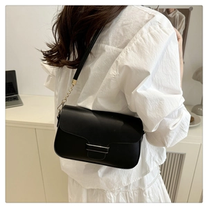 Detail of vintage black crossbody bag with metal buckle and gold chain strap in office setting