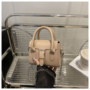 Detailed view of a beige leather mini handbag with a metal chain on a silver chair