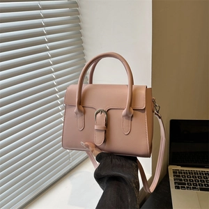 Pink faux leather crossbody bag with silver buckle and top handle in a lifestyle setting