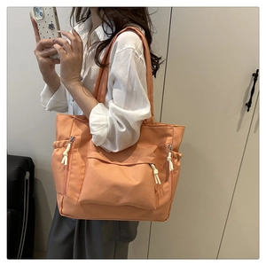 Side view of large orange tote bag with front zipper pocket and drawstring side detail